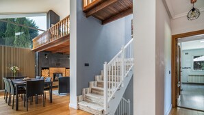 A spacious living area with a wooden floor, a dining table, and a staircase with white railings.