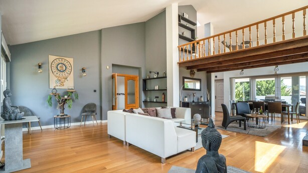 A spacious living area with a white sofa, a dining table, and a staircase leading to an upper level.