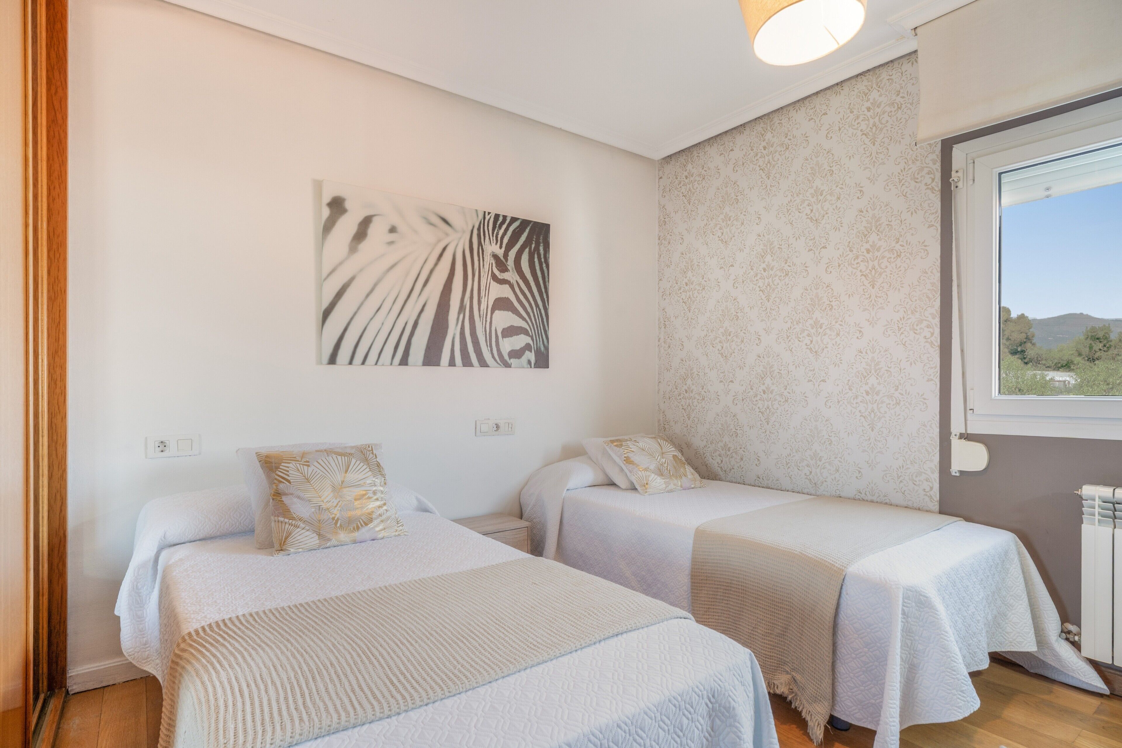 Quarto com duas camas, uma obra de arte com estampa de zebra na parede e janela com vista.