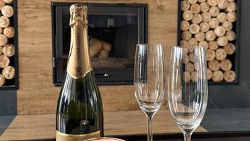 En træbakke med champagne, to glas og et lys på et bord foran en pejs.