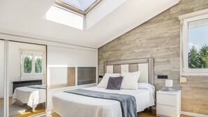 A bedroom with a large bed, a nightstand, a mirror, and a window with a view of trees.