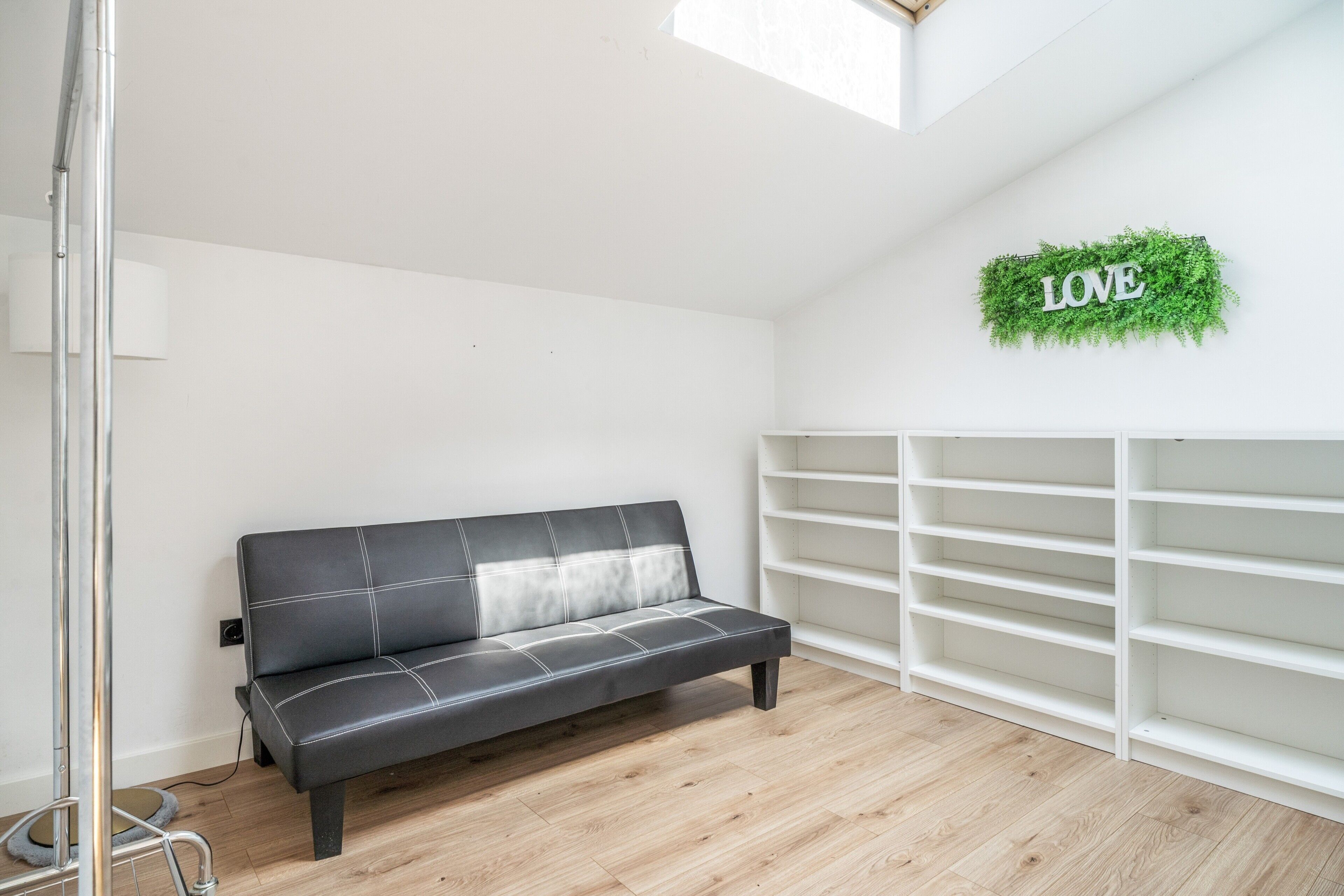 En moderne stue med en sort lædersofa, et hvidt indbygget reolsystem og et skilt med ordet 'LOVE' på væggen.