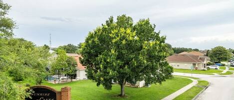 A residential area with a large tree in the foreground, a sign reading "Sunrise Lakes", and houses in the background.
