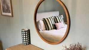 A wooden desk with a mirror, a vase with dried plants, and a bed with striped pillows in the background. - Charming countryside cottage near Canterbury, Kent (Bekesbourne)