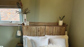A bedroom with a wooden headboard, white bedding, and a window with a view of a brick wall. - Charming countryside cottage near Canterbury, Kent (Bekesbourne)