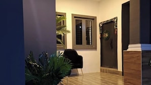 A modern interior with a wooden floor, a black chair, a potted plant, and a door with a wreath. - NPJ Luxury Apartment  (Uyo)