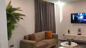 A modern living room with a sofa, two armchairs, a coffee table, a TV, and a large plant.