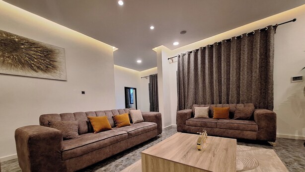 A modern living room with two sofas, a coffee table, and a large abstract painting on the wall. - NPJ Luxury Apartment  (Uyo)