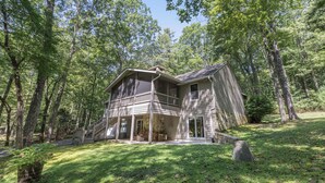 Une maison à deux étages avec un porche, entourée d’une zone boisée.