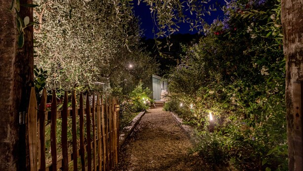 Un chemin de jardin éclairé, bordé d’une clôture en bois et de lampes décoratives.