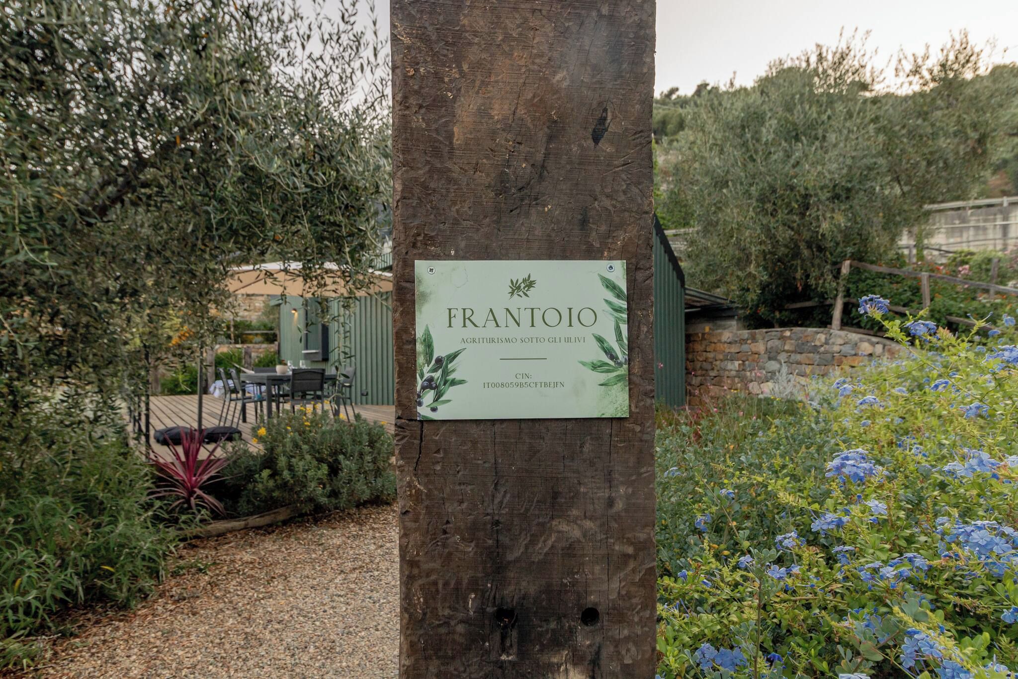 A sign on a tree with the name 'FRANTOIO' and a description of agriturismo.