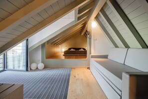 Een zolderkamer met hoge plafonds, een schuine kap, een ingebouwd bed en een groot raam.