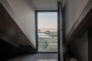A narrow, sloped room with a large window overlooking a residential area.