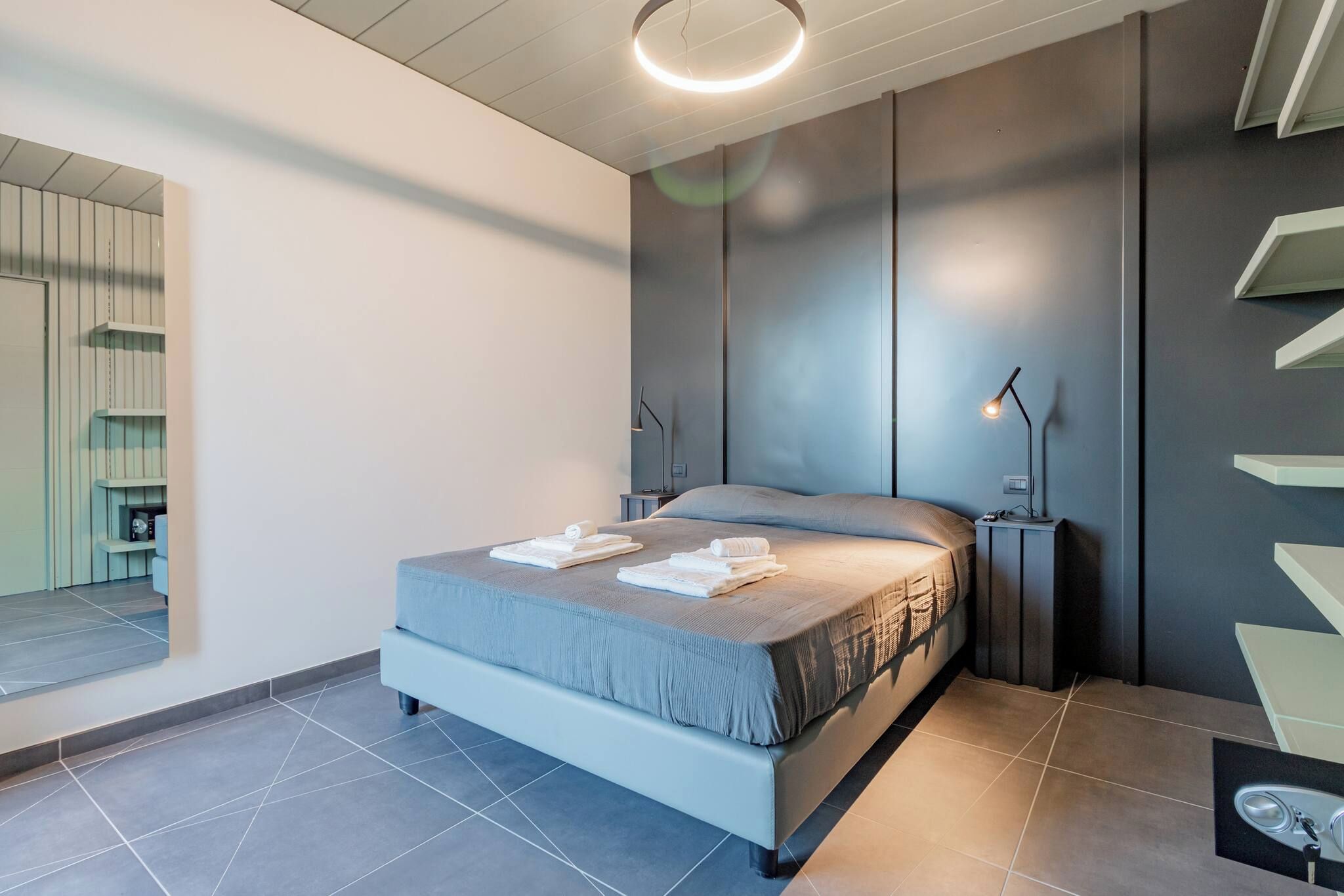 A modern bedroom with a bed, bedside lamps, and a built-in shelf unit.
