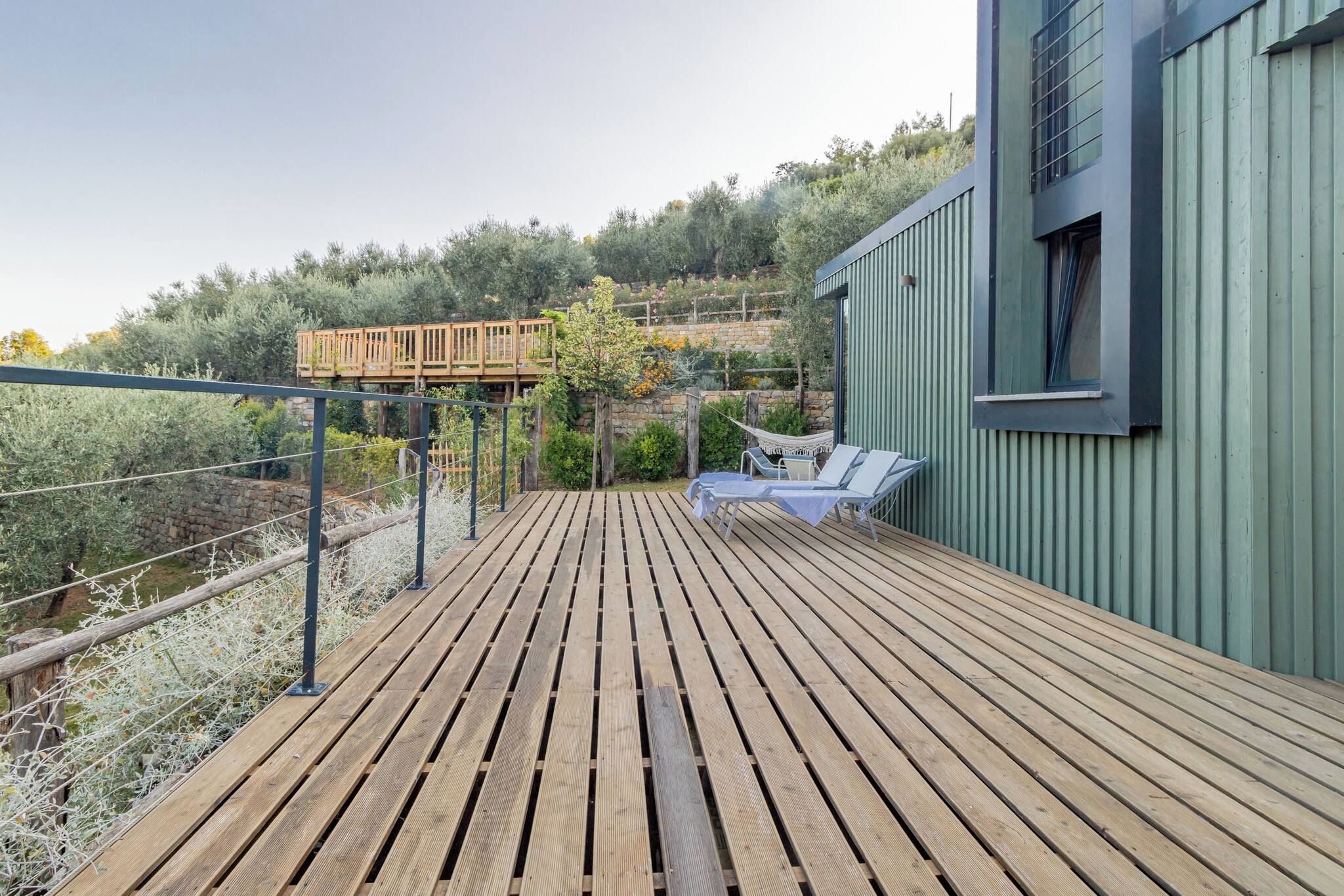 A wooden deck with a view of a hillside garden, a small wooden bridge, and a building with a window.