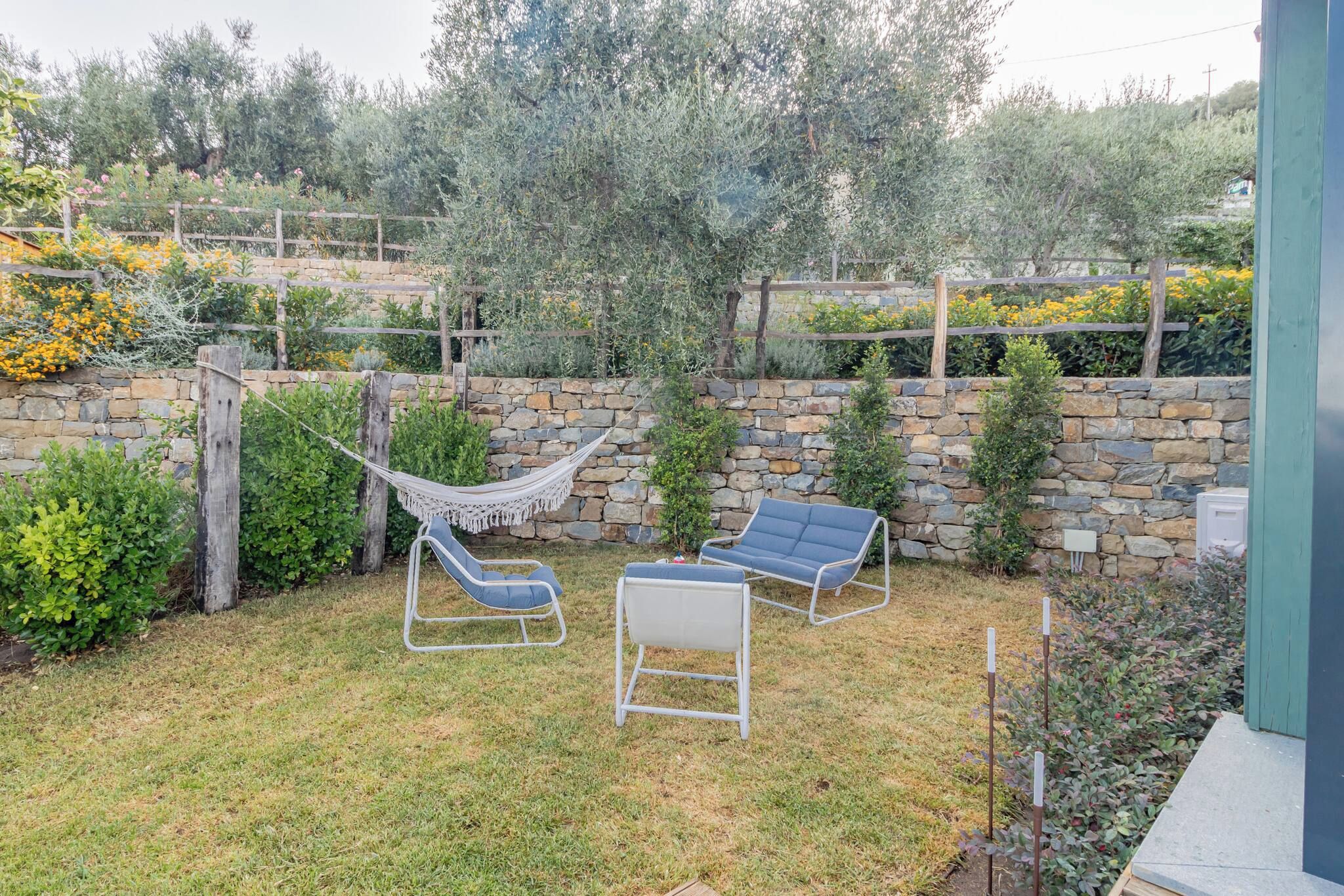A backyard with a stone wall, a hammock, and two lounge chairs.