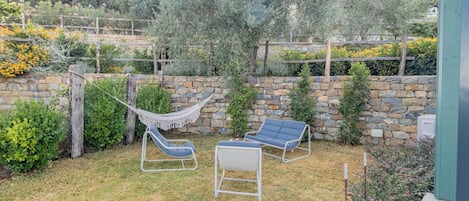 A backyard with a stone wall, a hammock, and two lounge chairs.