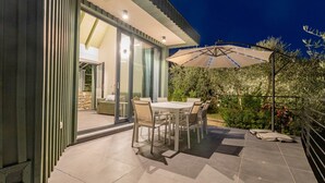 Une terrasse extérieure avec une table et des chaises, un grand parasol et une vue sur un jardin.