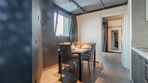Un espace de salle à manger moderne avec une table dressée pour quatre personnes, une fenêtre avec des rideaux et une vue sur une autre pièce.