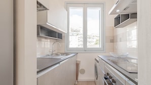 A compact kitchen with a window, built-in appliances, and a view of the city.