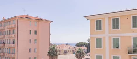 A multi-story building with balconies, a visible storefront, and a clear view of the sea in the background.