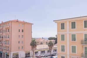 A multi-story building with balconies, a visible storefront, and a clear view of the sea in the background.