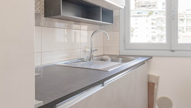 A modern kitchen with a stainless steel sink, a window above the sink, and a view of the cityscape.