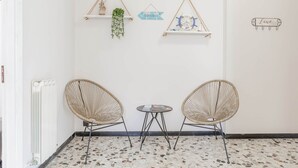 Ein Zimmer mit zwei Korbstühlen, einem kleinen runden Tisch, einem Heizkörper und drei Wanddekorationen.
