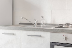 A kitchen with a stainless steel sink, a soap dispenser, and a stove.