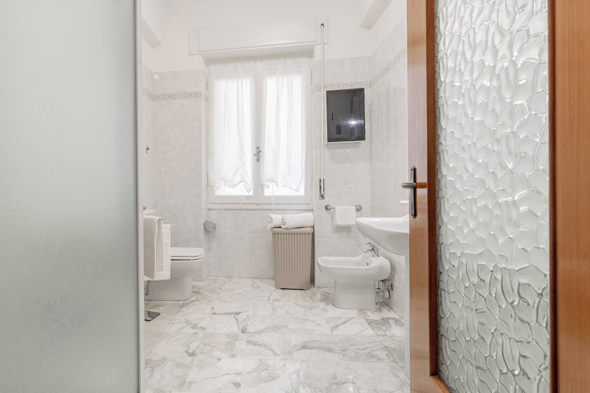 Ein Badezimmer mit Toilette, Bidet und Waschbecken, ein Fenster mit Vorhängen und einer Wand mit Muster.