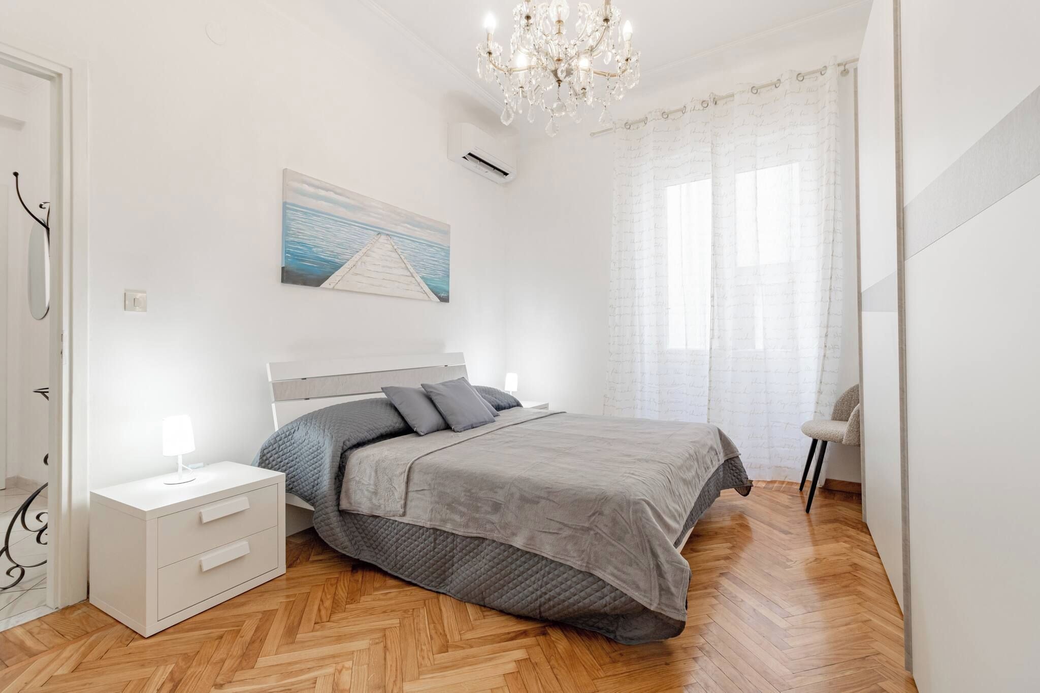 Een slaapkamer met een bed, nachtkastjes, een hanglamp, een schilderij en een raam met gordijnen.