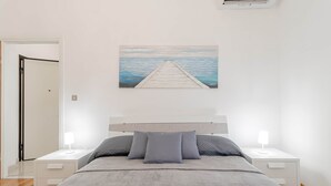 A bedroom with a bed, two bedside tables, a nightstand, a door, and a painting of a pier. - Route 66 - Sea and Beaches (Sanremo)