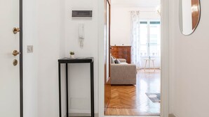 A hallway with a door, a wall-mounted phone, a small table with a plant, and a sofa in the background. - Route 66 - Sea and Beaches (Sanremo)
