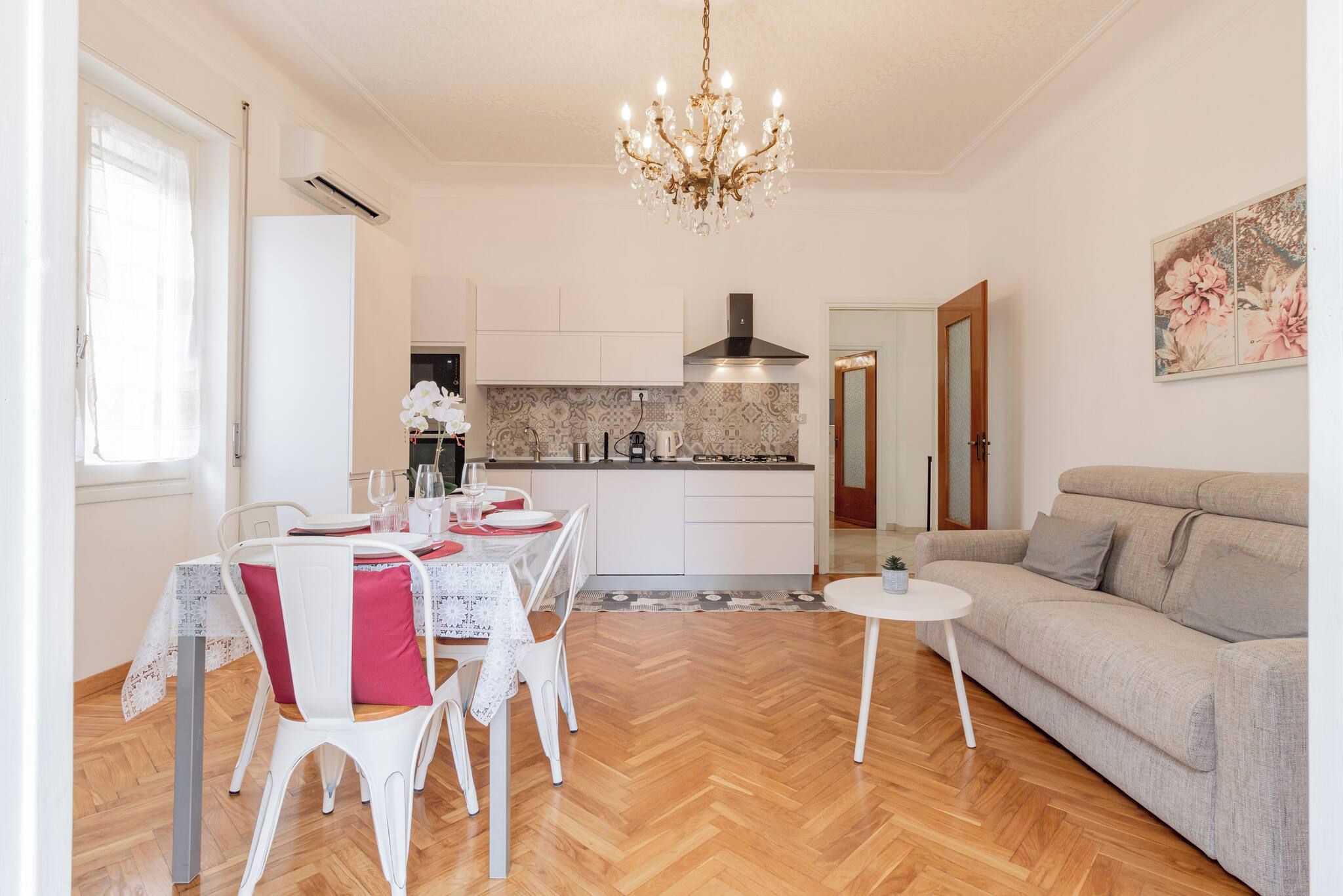 Een moderne woonkamer met een eethoek, een kroonluchter en een keuken op de achtergrond.