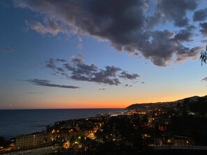 A coastal cityscape at dusk with a view of the sea and a town with illuminated buildings. - AGAVE VICTORIAE REGINAE APARTMENT - Vista mare (Sanremo)