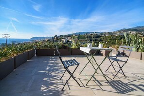 An outdoor terrace with a table and chairs, a view of a coastal landscape, and cacti. - AGAVE VICTORIAE REGINAE APARTMENT - Vista mare (Sanremo)