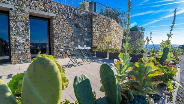 A stone building with a balcony, outdoor seating, and various plants.