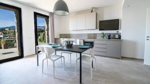 A modern kitchen with a dining area, large windows, and a view of the landscape.