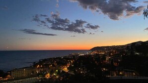 A coastal cityscape at dusk with a view of the sea and a distant mountain range.