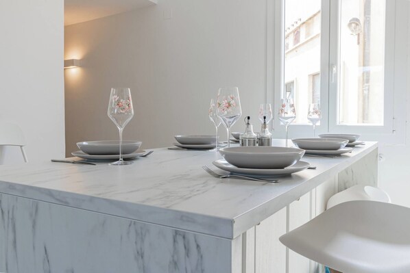Un comedor moderno con encimera de mármol, sillas blancas y copas de vidrio con motivos florales.
