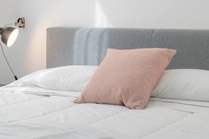 A bed with a grey headboard, white bedding, and a single patterned pillow.