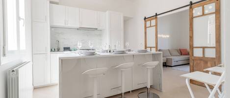 A modern kitchen with white cabinets, a marble countertop, and three bar stools.