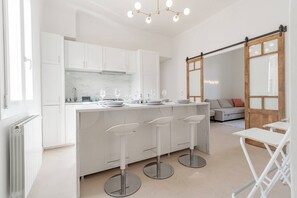 Cocina moderna con alacenas blancas, encimera de mármol y tres taburetes de bar.