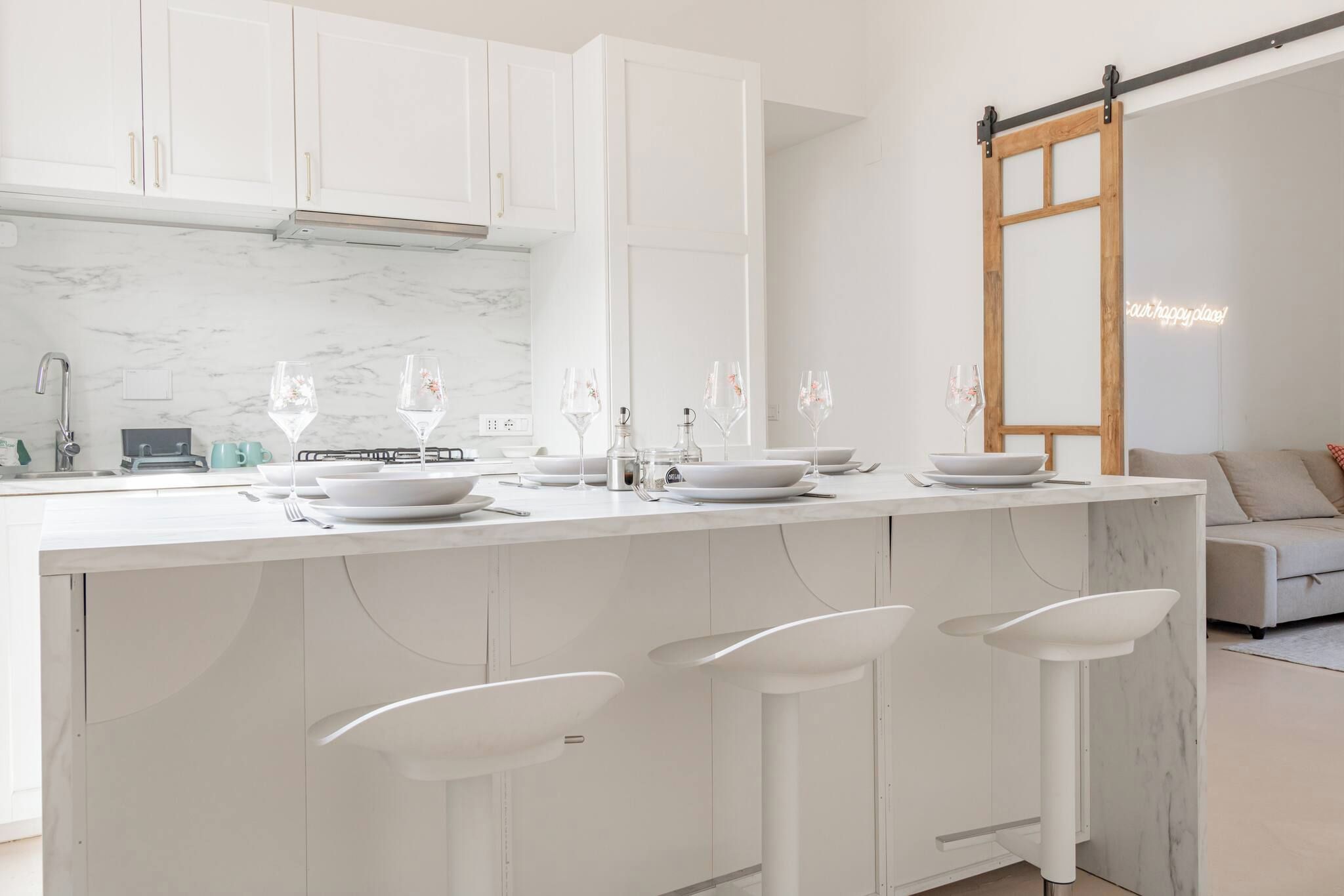 A modern kitchen with white cabinetry, a marble countertop, and bar stools.