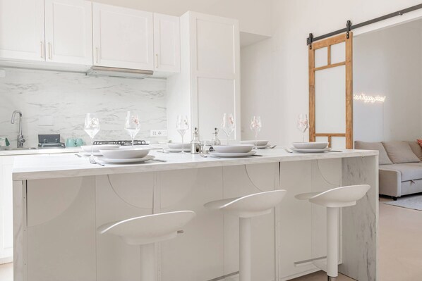 A modern kitchen with white cabinetry, a marble countertop, and bar stools.