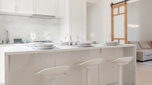 Eine moderne Küche mit weißen Schränken, einer Marmor-Spritzschutzwand und einer zentralen Kochinsel mit Barhocker.