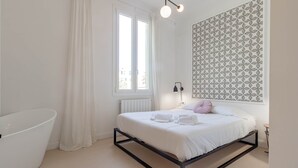 Ein modernes Schlafzimmer mit einem Bett, einer weißen Badewanne und einem Fenster mit Vorhängen.