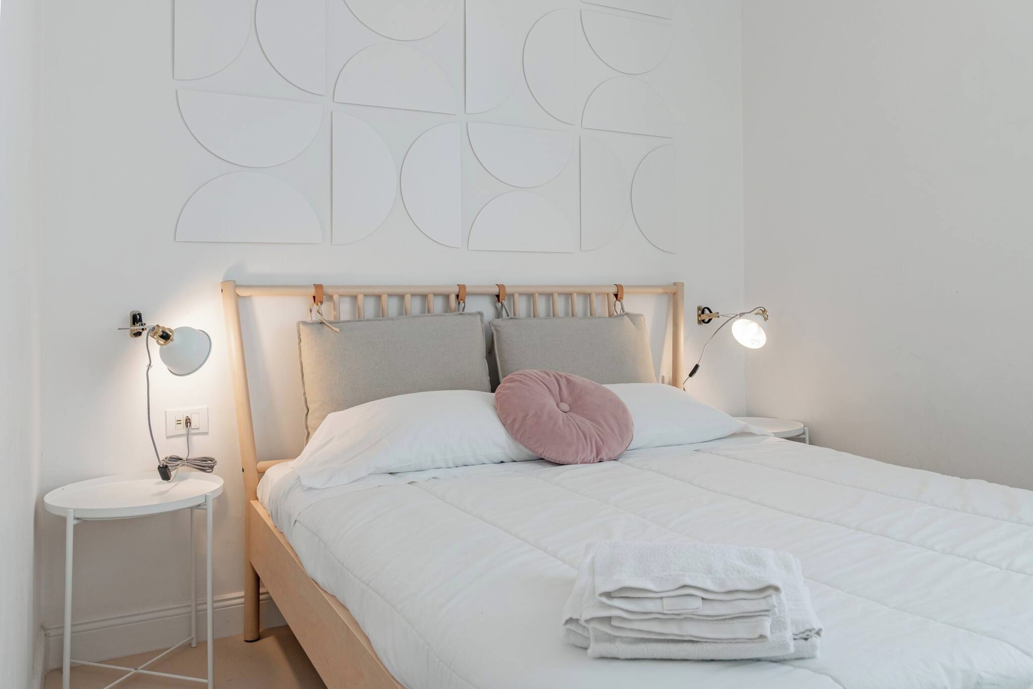 A bedroom with a bed, bedside tables, a wall-mounted light, and a wall decoration.