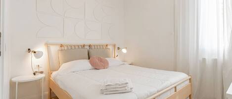 A bedroom with a wooden bed, a bedside table, a lamp, and a wall with abstract art.