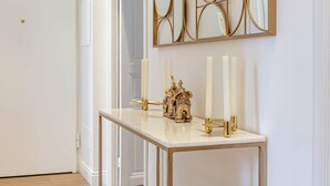 Une console blanche avec un cadre doré, des bougies blanches et une statuette d’éléphant dorée.